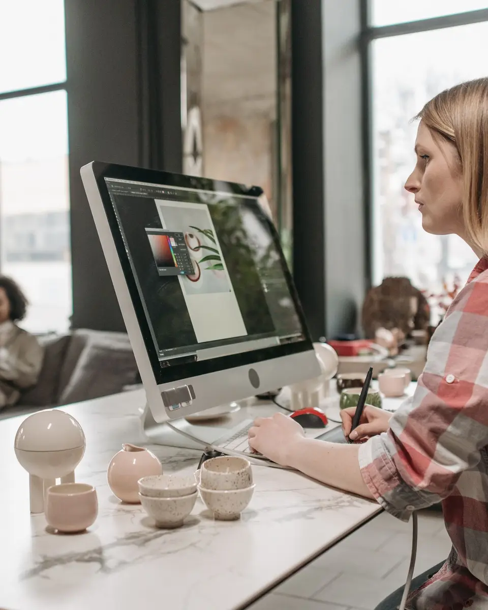 A designer in a plaid shirt edits a layout on a large desktop monitor in a bright loft studio