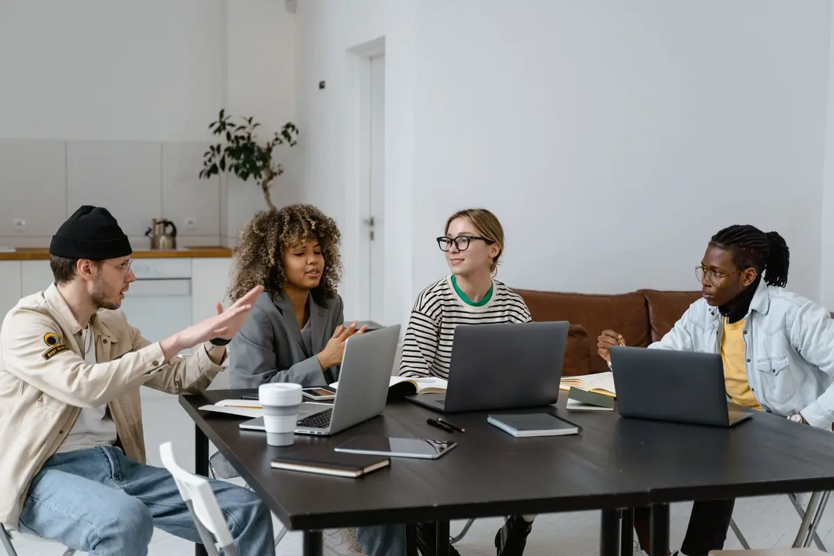 Four colleagues talking around a table with laptops in a bright office