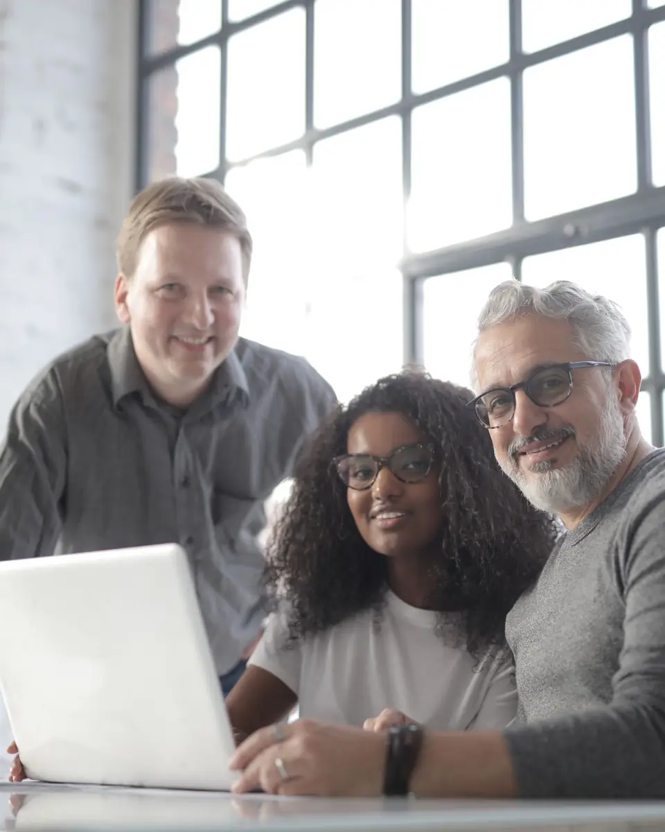 Three colleagues smiling at a laptop in a bright office