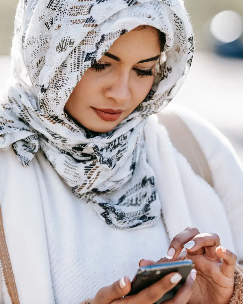 Woman in a patterned headscarf typing a message on her phone