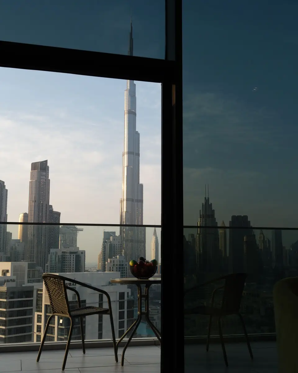 The Burj Khalifa and Downtown Dubai towers seen from an apartment balcony with two chairs, at dusk
