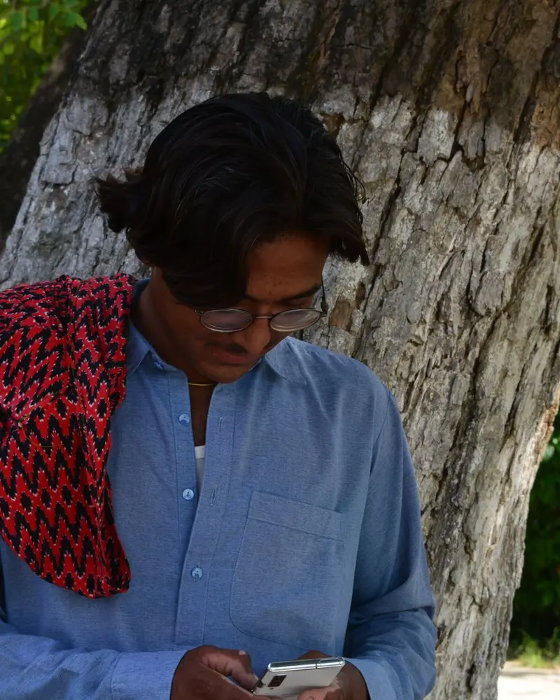 Young man in a blue kameez with a red shawl reading a WhatsApp reply on his phone