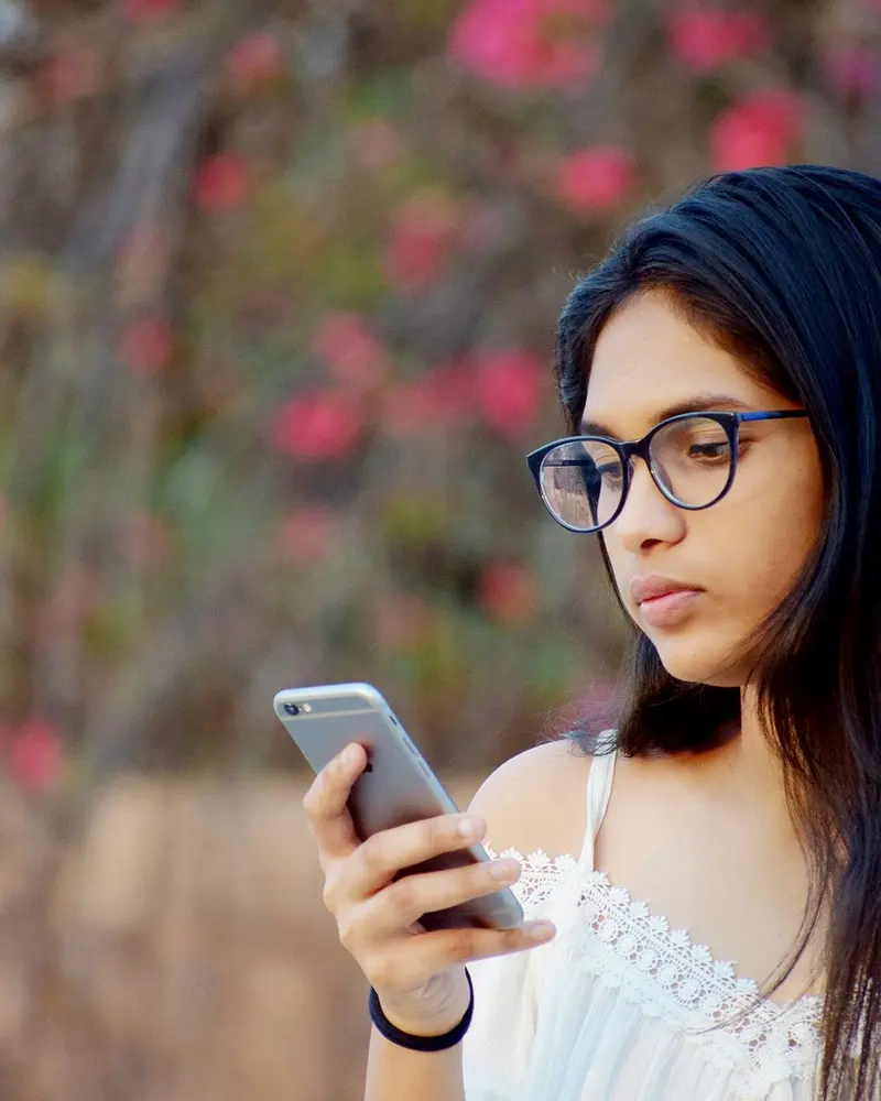 Young woman in glasses reading a reply on her phone outdoors